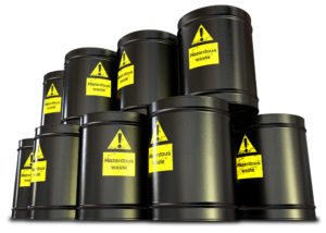 A stack of black metal barrels with yellow hazardous waste drum labels on each
